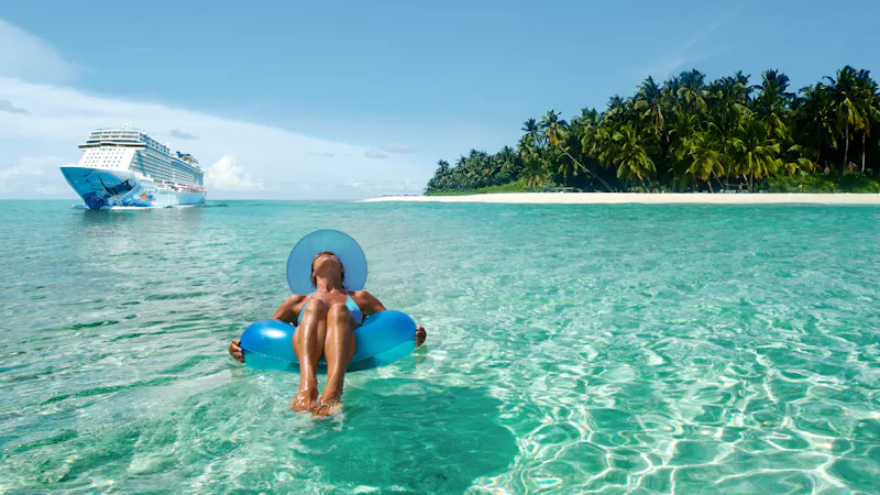 Woman lying on an inflatable in the Caribbean ocean with an NCL ship in the background